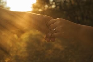 Silhouetted hands reaching toward each other against a golden sunset sky.