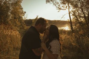 Couple embracing outdoors during golden hour with autumn foliage in background.