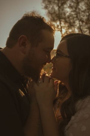 Romantic couple sharing an intimate moment in golden sunset lighting with trees in background.