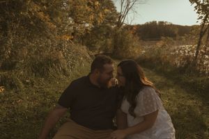 Couple embracing on grassy hillside with autumn trees in background.