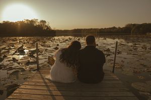 Silhouettes of a couple sitting by a lake at sunset with lily pads in view.