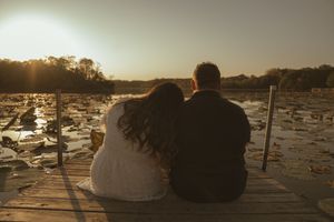 Two people sit close together on a wooden dock at dusk.