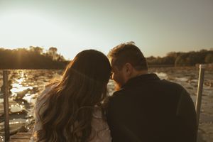 A couple sits together on a dock during golden hour overlooking a serene lake.