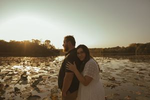 A romantic moment shared between two people on a lakeside dock at sunset.