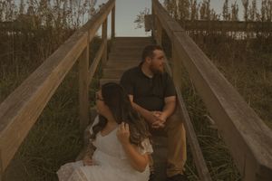 A couple shares an intimate moment on a wooden walkway surrounded by nature.