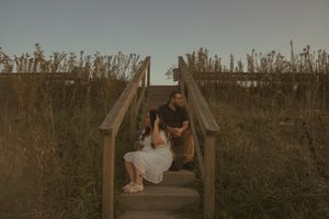 A couple embraces on a wooden boardwalk during golden hour.