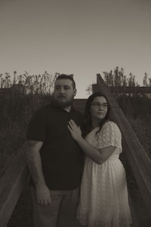 A couple poses together on a wooden boardwalk in black and white.