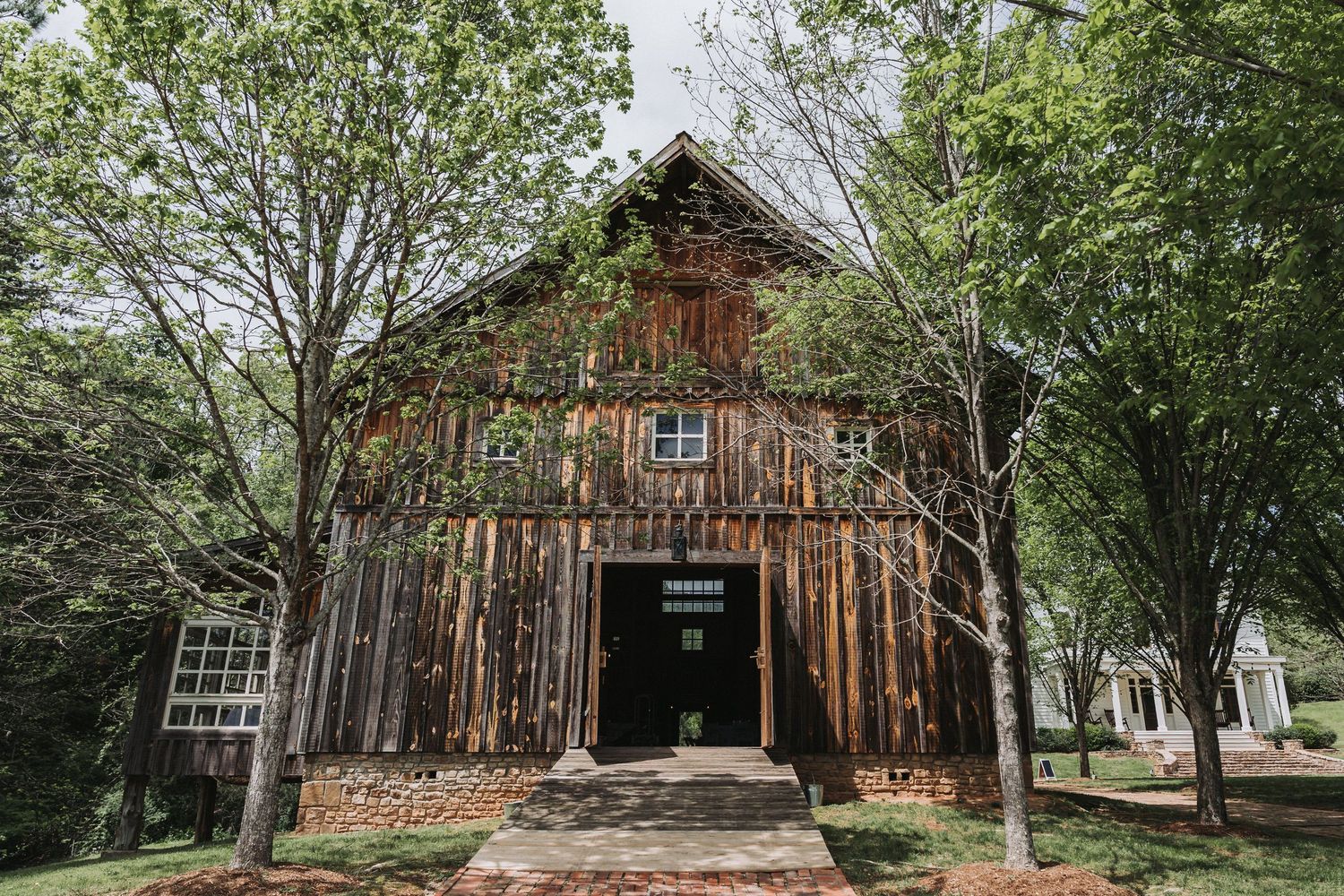 Rustic wooden barn with weathered siding surrounded by trees and natural landscaping at a historic property.