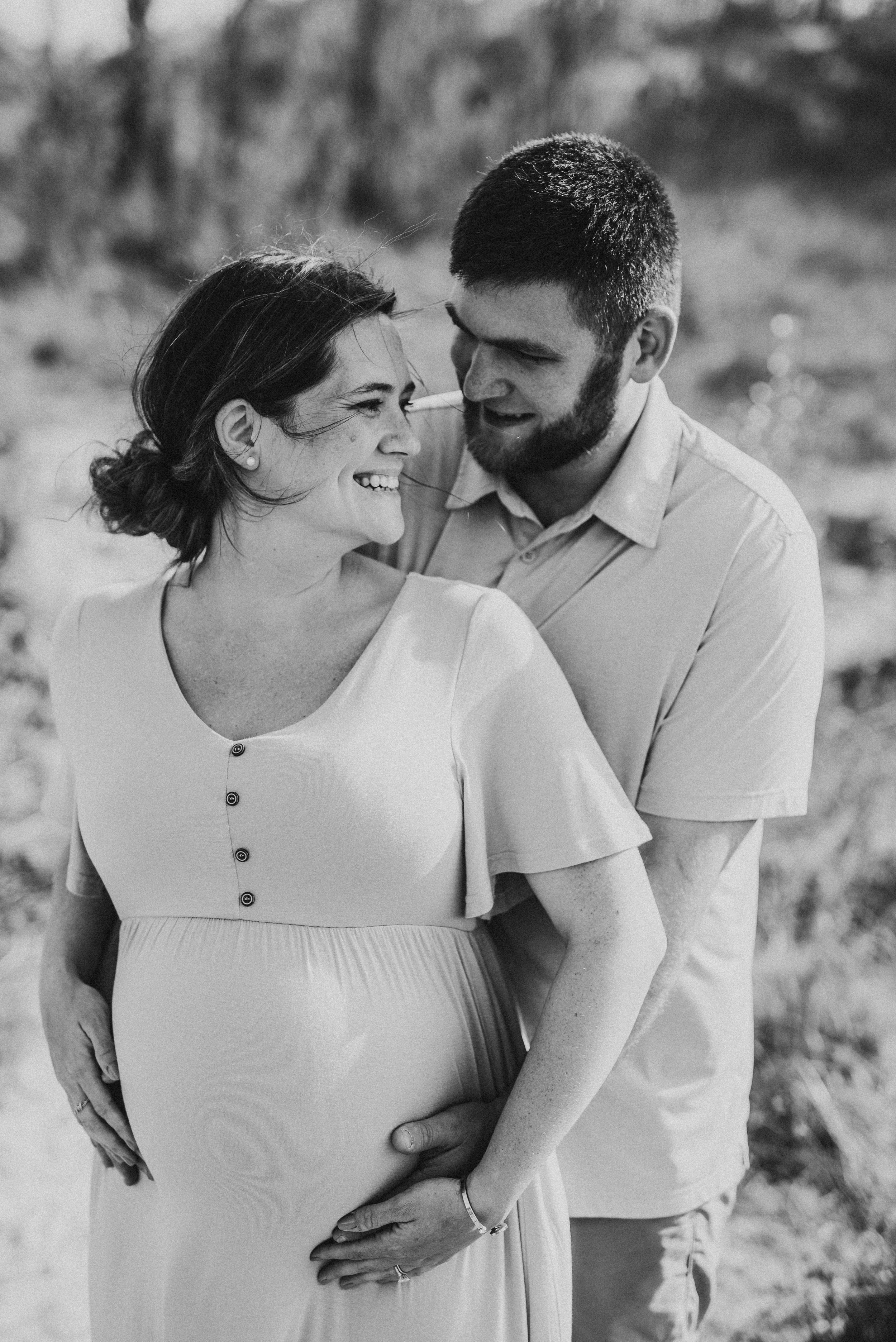 A couple shares an intimate moment during a maternity photoshoot in black and white.