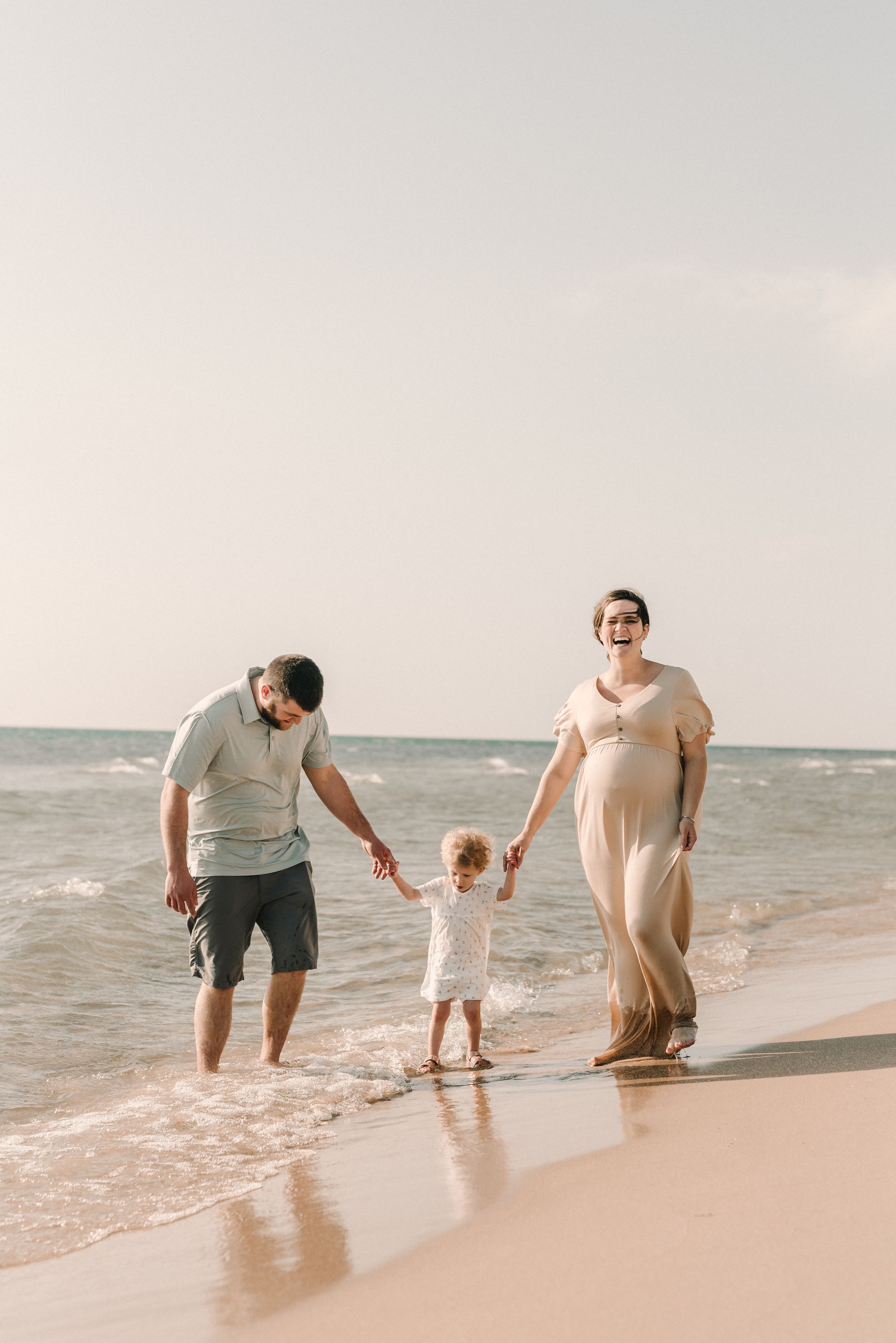 Family walking together on a sandy beach at sunset with waves lapping at their feet.