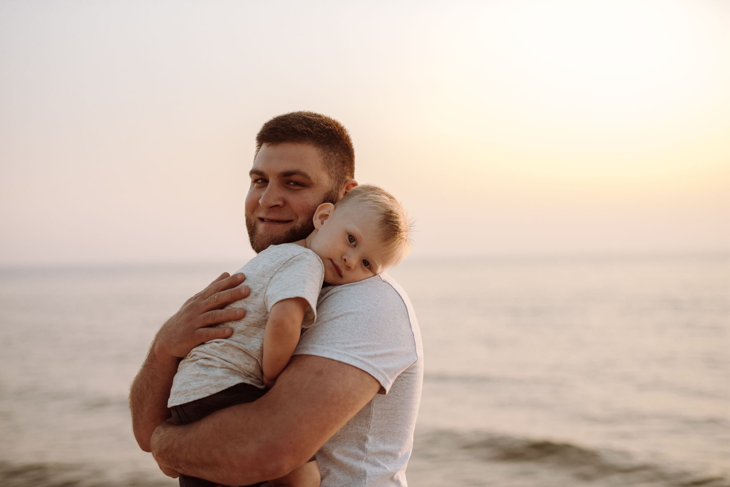 A tender embrace between parent and child silhouetted against a peaceful sunset over the ocean.