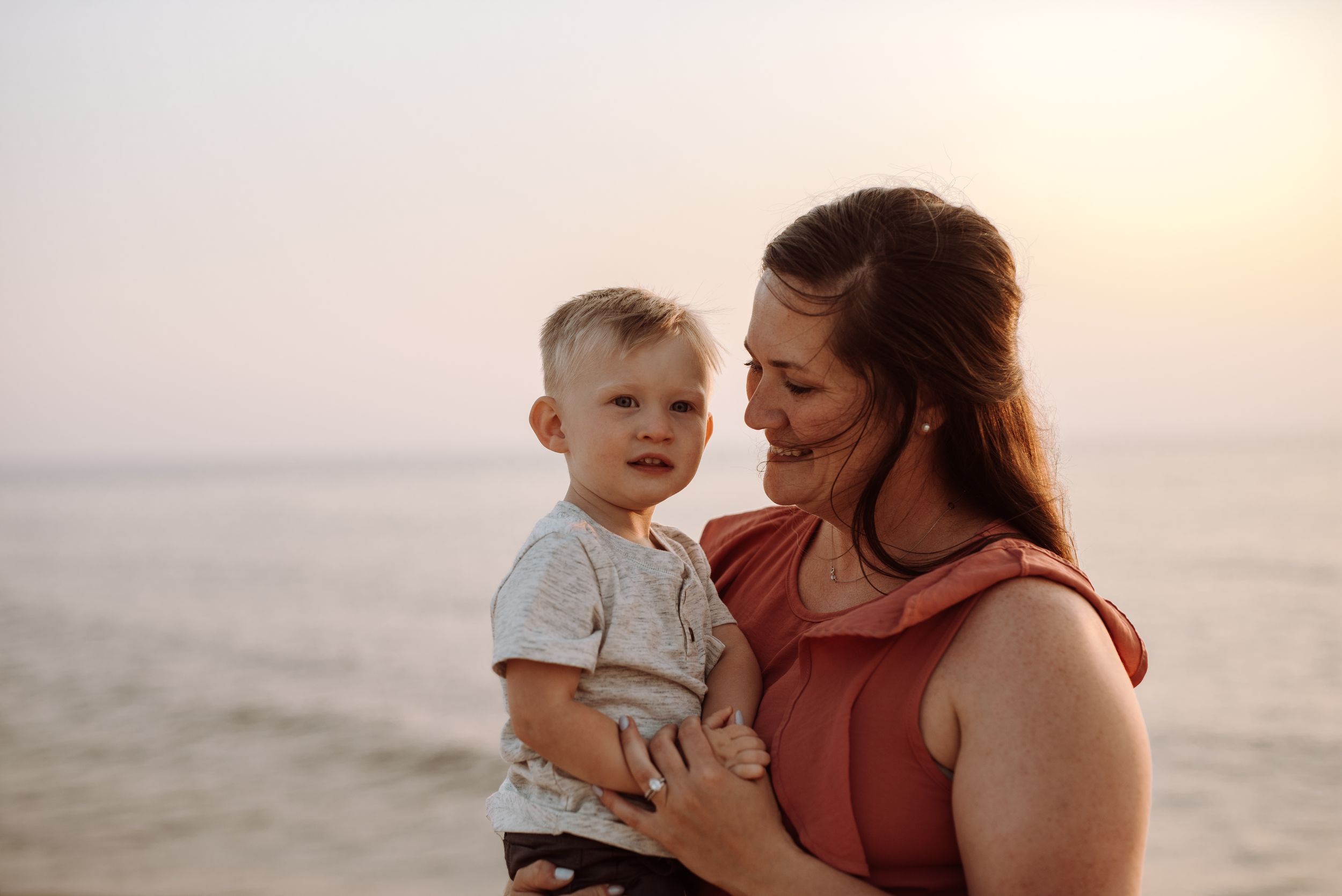 Parent and toddler share tender moments at sunset on the beach with warm golden light behind them.