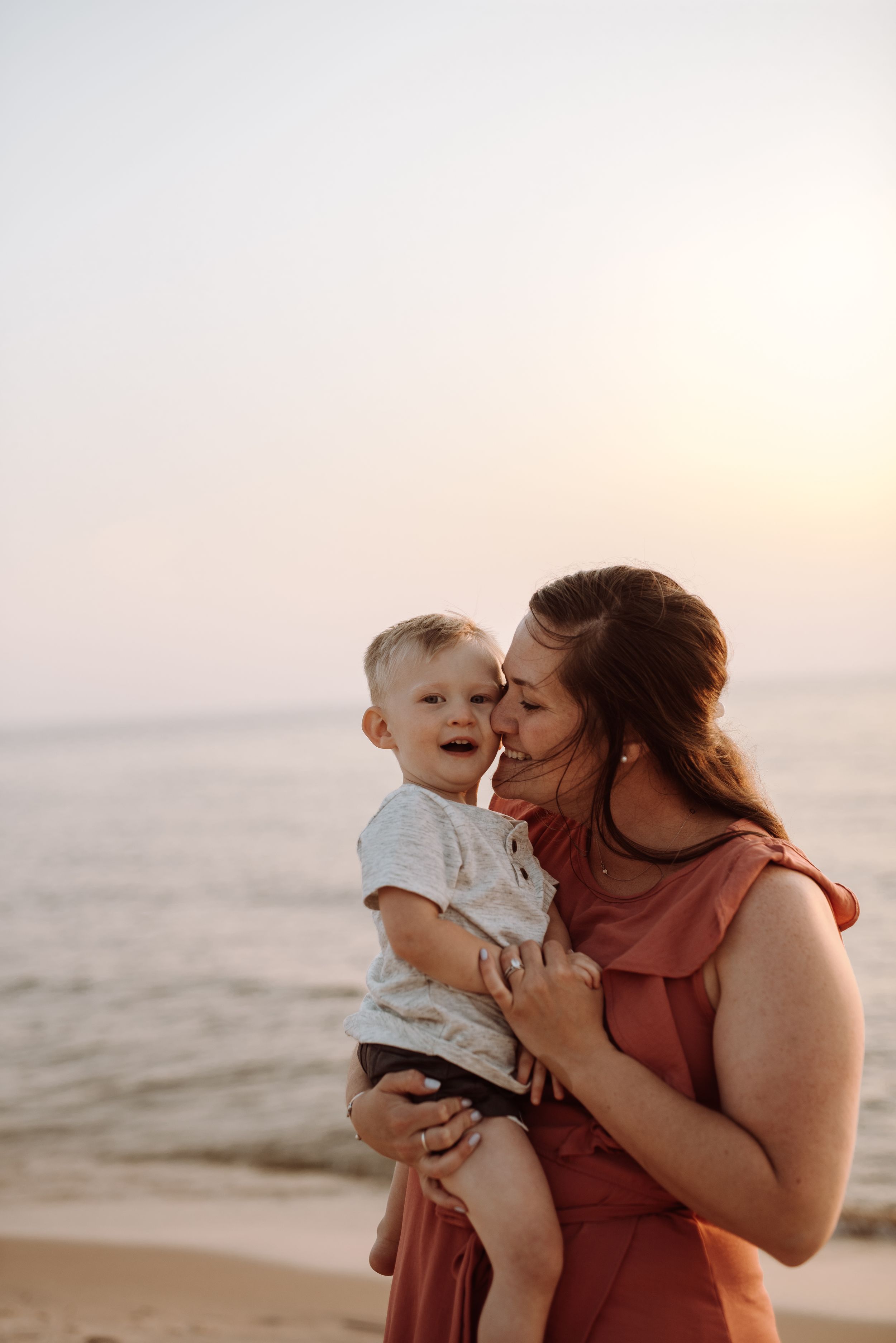 Two people share a tender moment at sunset on a beach with golden light illuminating the scene.