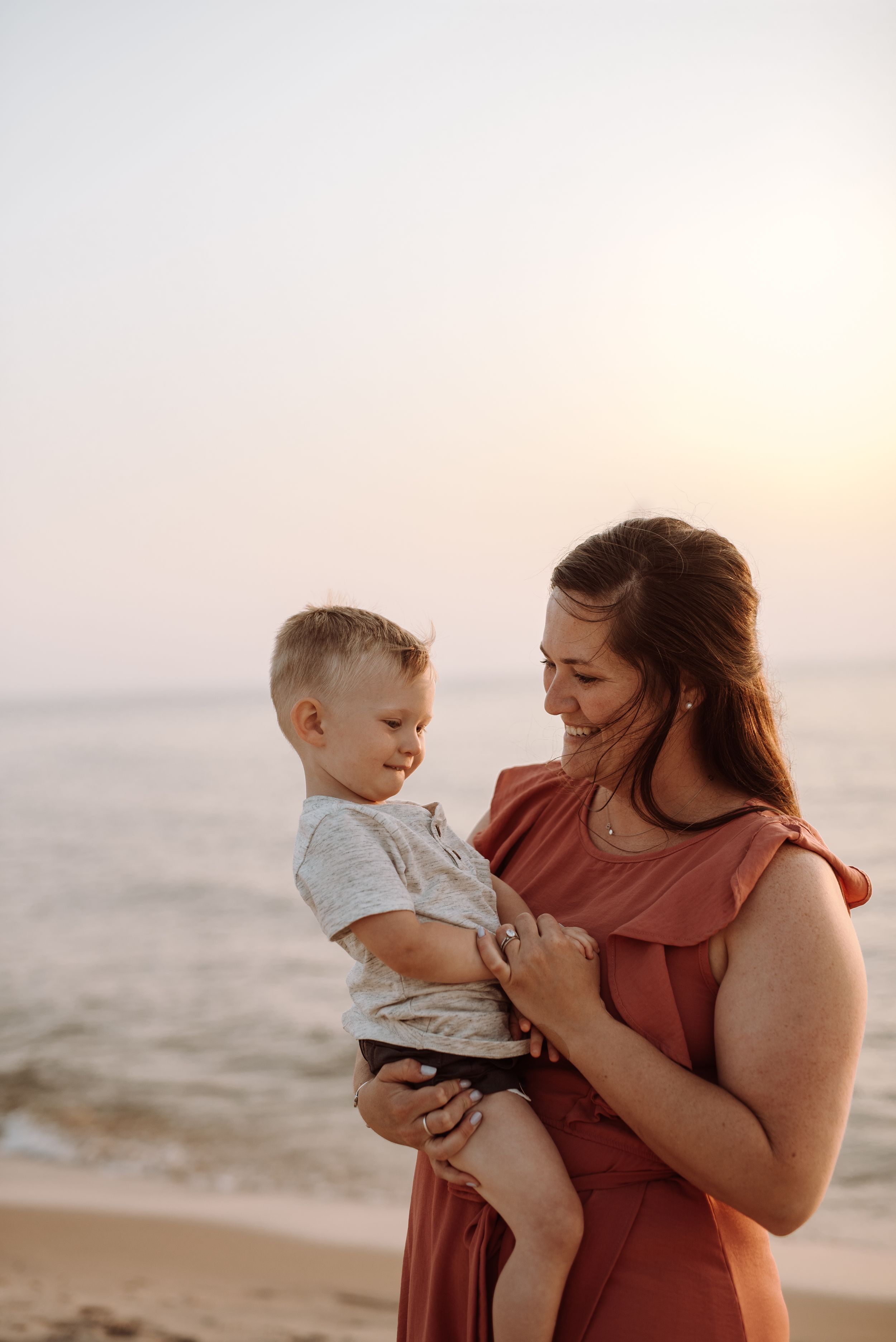 Parent and child share tender moments on the beach during golden hour at sunset.
