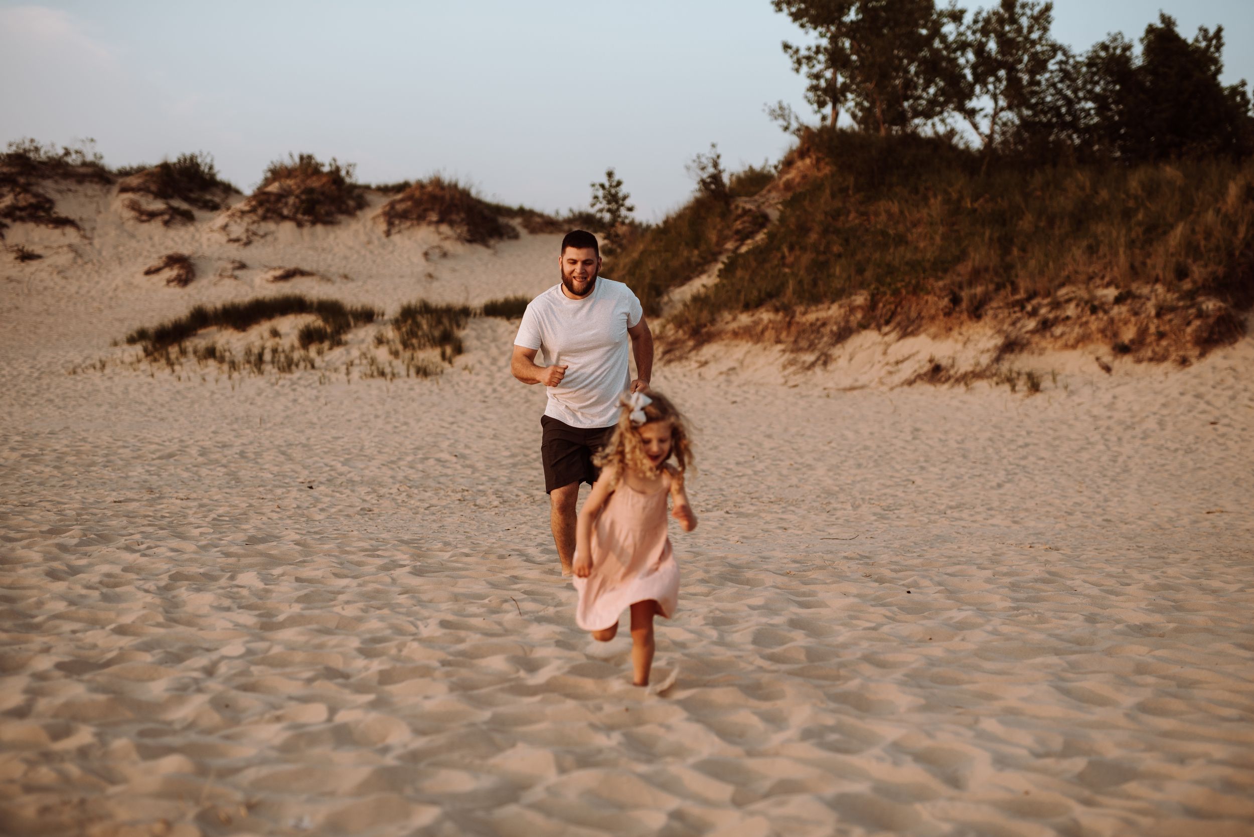 People running joyfully together on sandy beach dunes during golden sunset light.