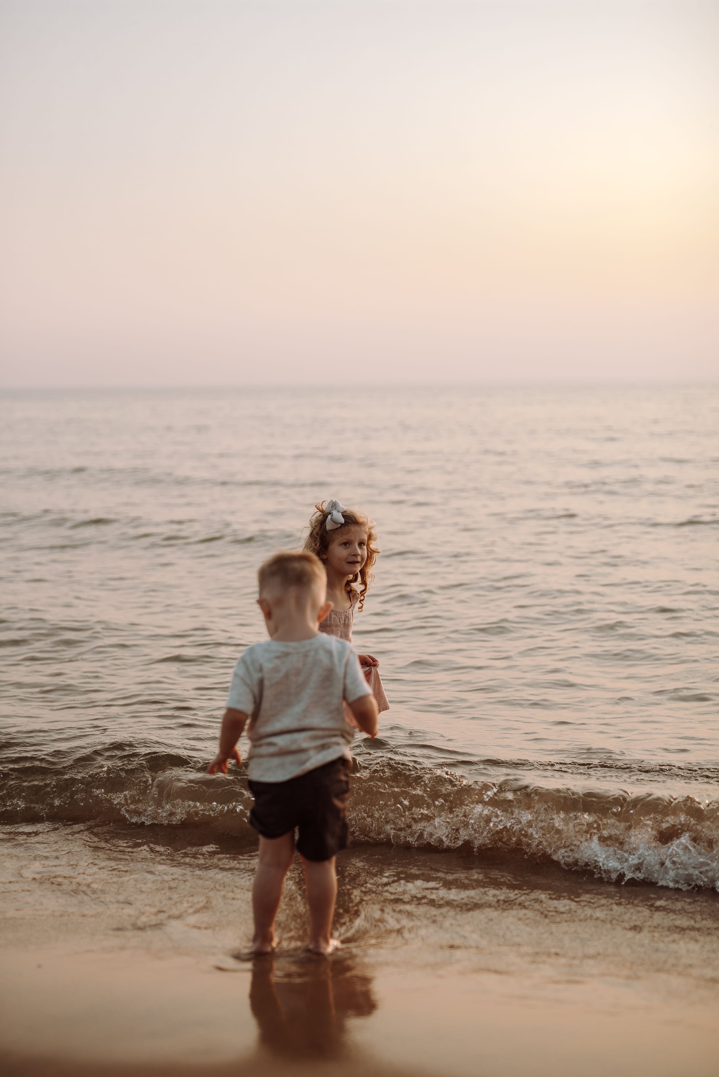 Two children play in the ocean waves at sunset on a peaceful beach.