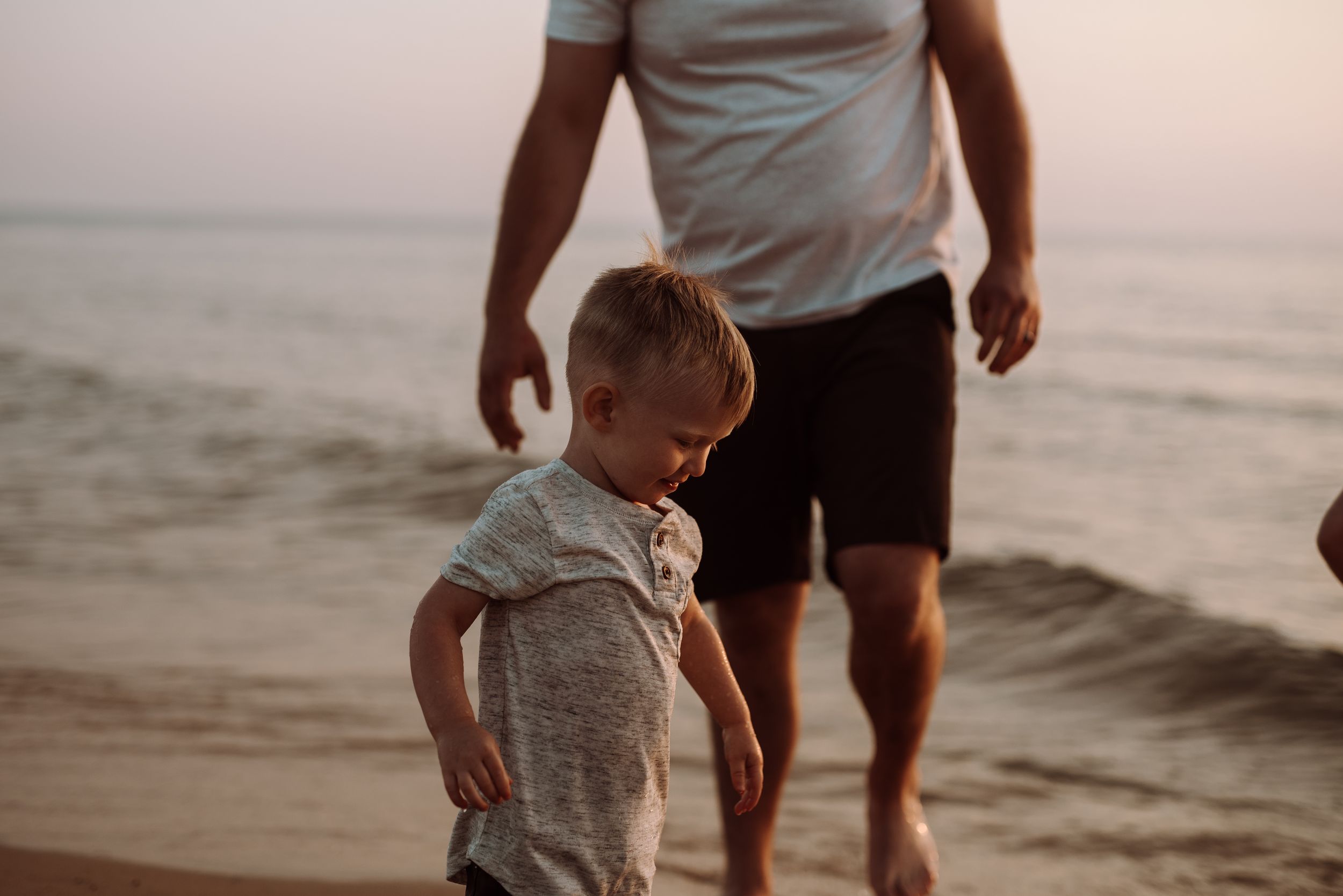 Family walking together and playing on a sandy beach at sunset with waves lapping at their feet.