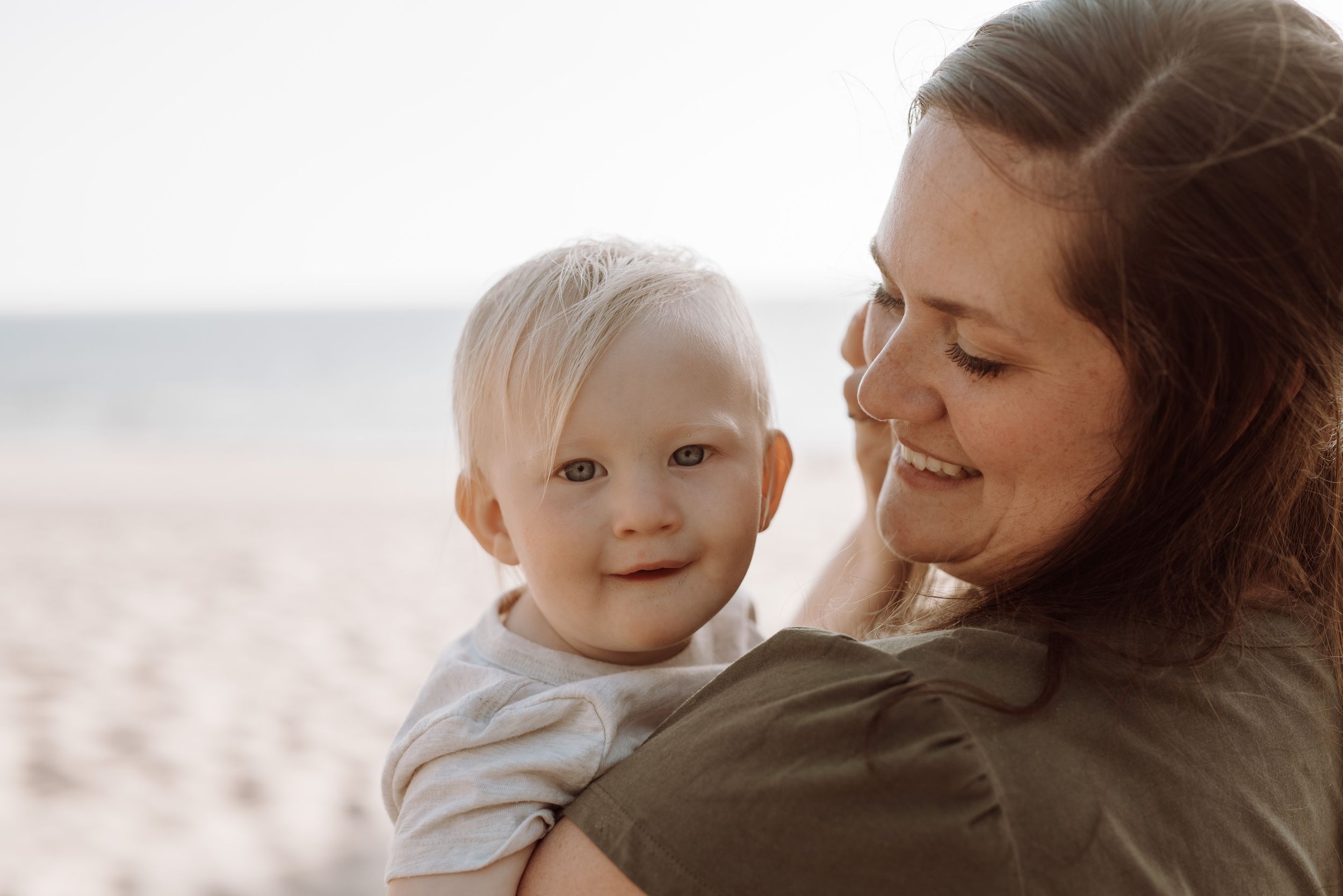 A parent holds a smiling baby against a soft blurred background at sunset.