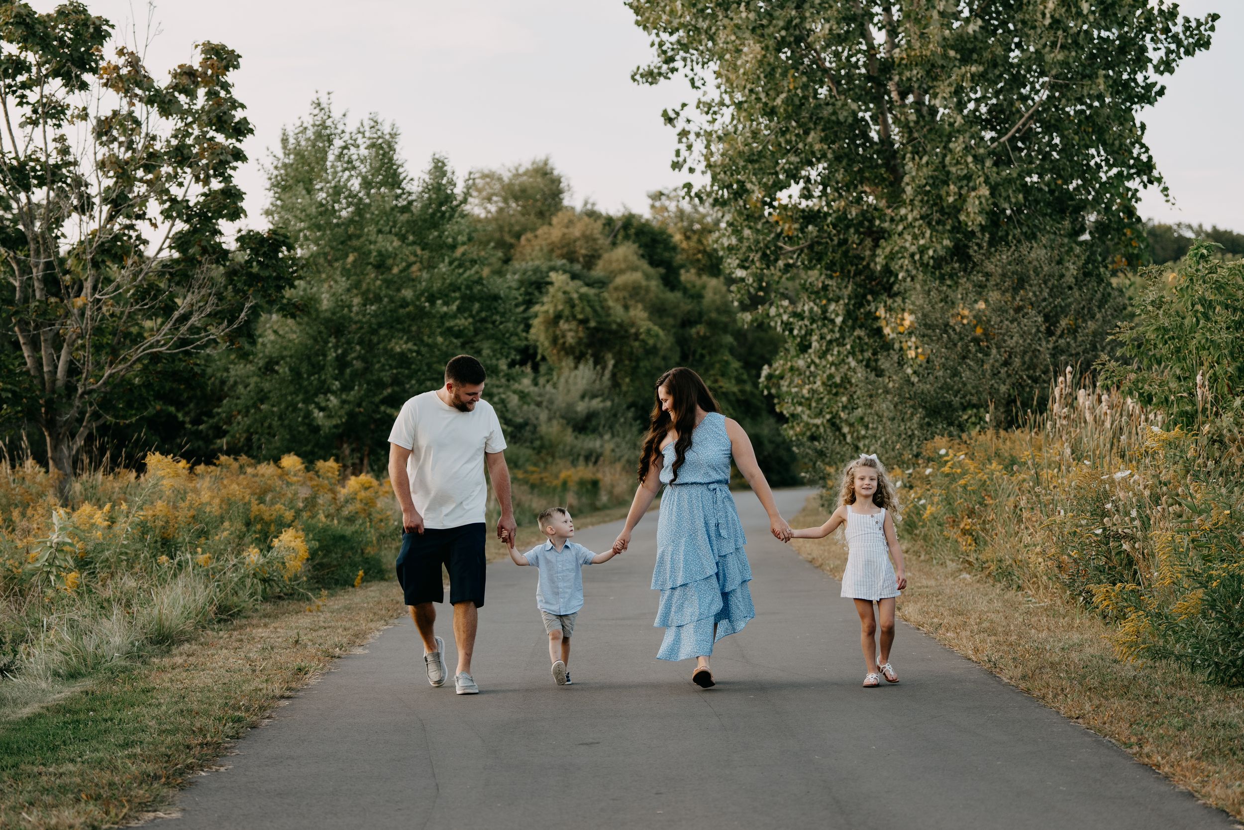 Family takes a leisurely stroll together on a tree-lined country path during a sunny summer day.