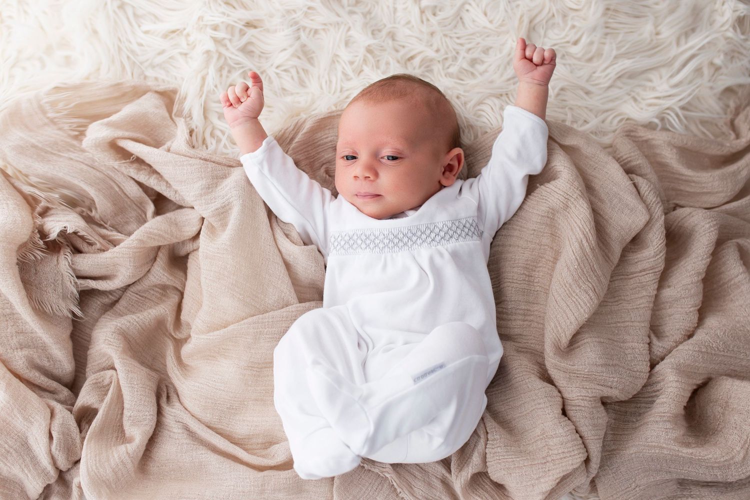 newborn baby in baby grow, lay on blanket with arms outstretched by little wonderland photography widnes cheshire