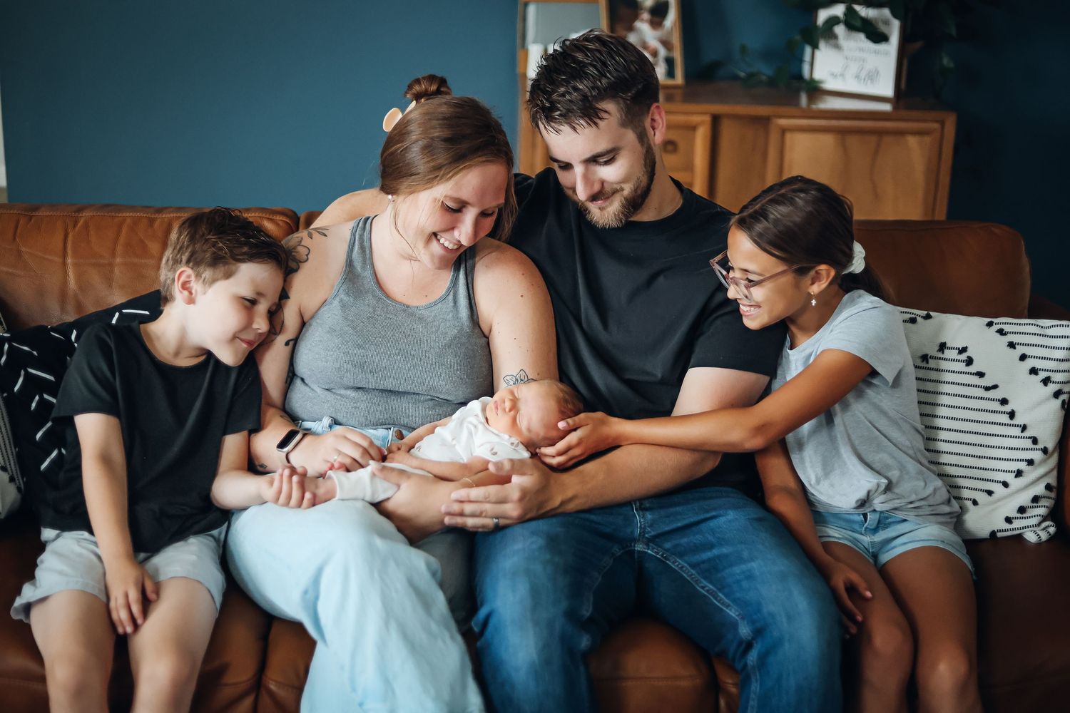 Family sitting close together on a couch for casual indoor photos. Family style newborn photography