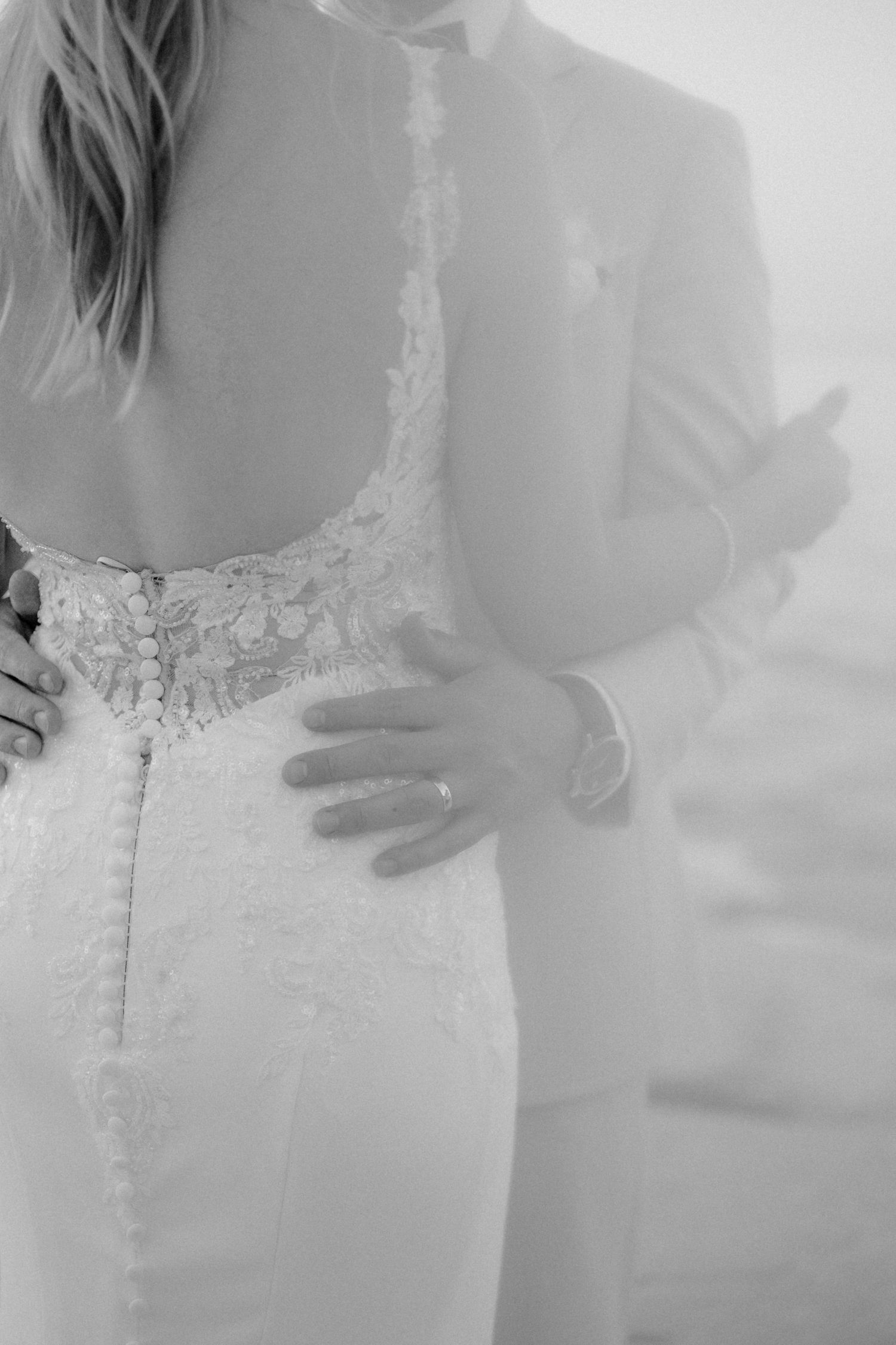 Close-up black and white detail of intricate lace wedding dress back with hands.