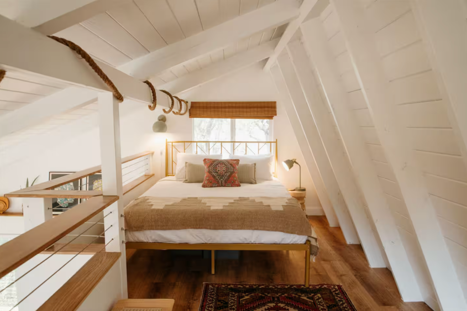 Modern attic bedroom features white vaulted ceiling, exposed beams, and custom built-in storage solutions with warm lighting.