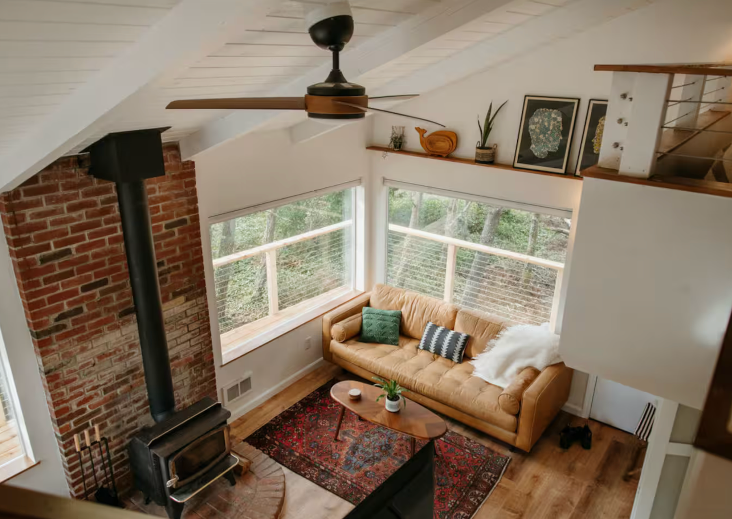 Cozy modern cabin interior with wood stove, leather sofa, oriental rug, and large windows overlooking nature.