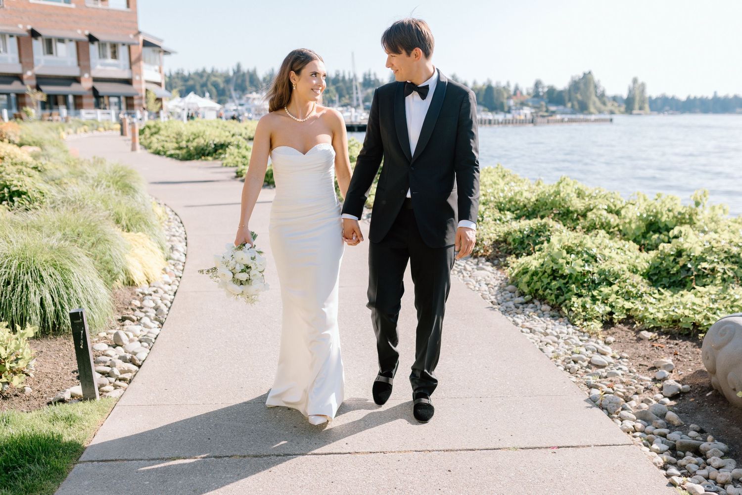 A couple walks hand in hand along a scenic waterfront path on their wedding day.