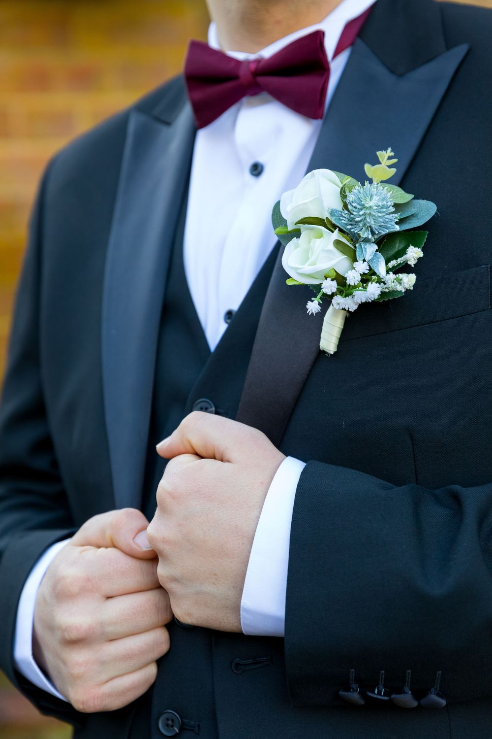Close-up of groom's burgundy bow tie and white boutonnière