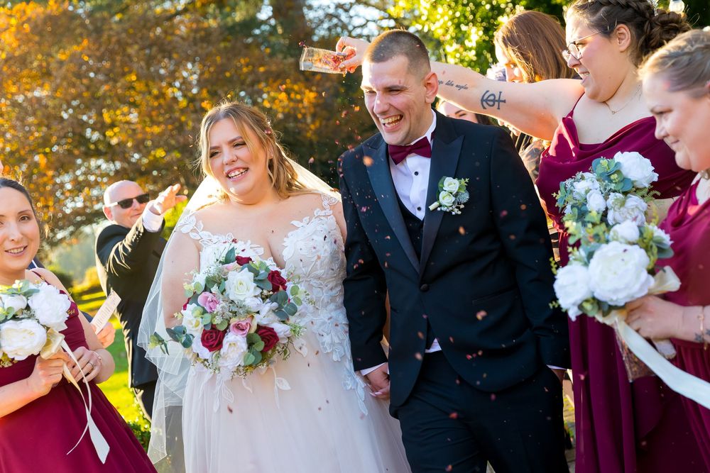 Katie and Ben smiling joyfully as guests shower them with confetti outside Audley’s Wood Hotel.