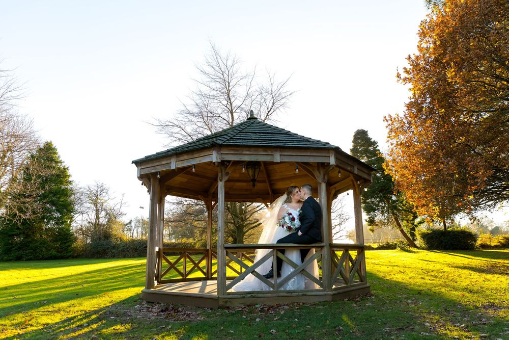 Romantic newlywed kiss under the wooden gazebo at Audley’s Wood Hotel, surrounded by golden autumn light.
