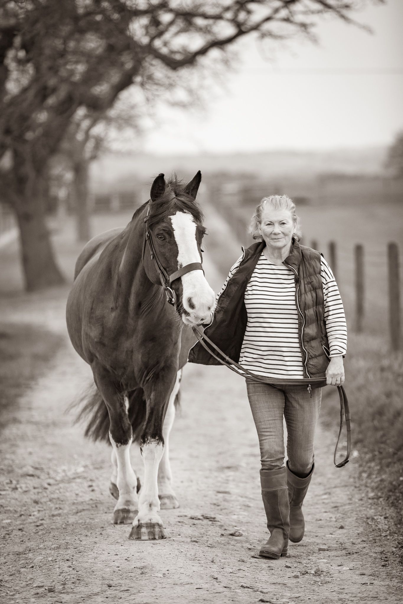 A gentle moment between a rider and dark horse with white blaze in a rustic stable setting, captured in black and white.