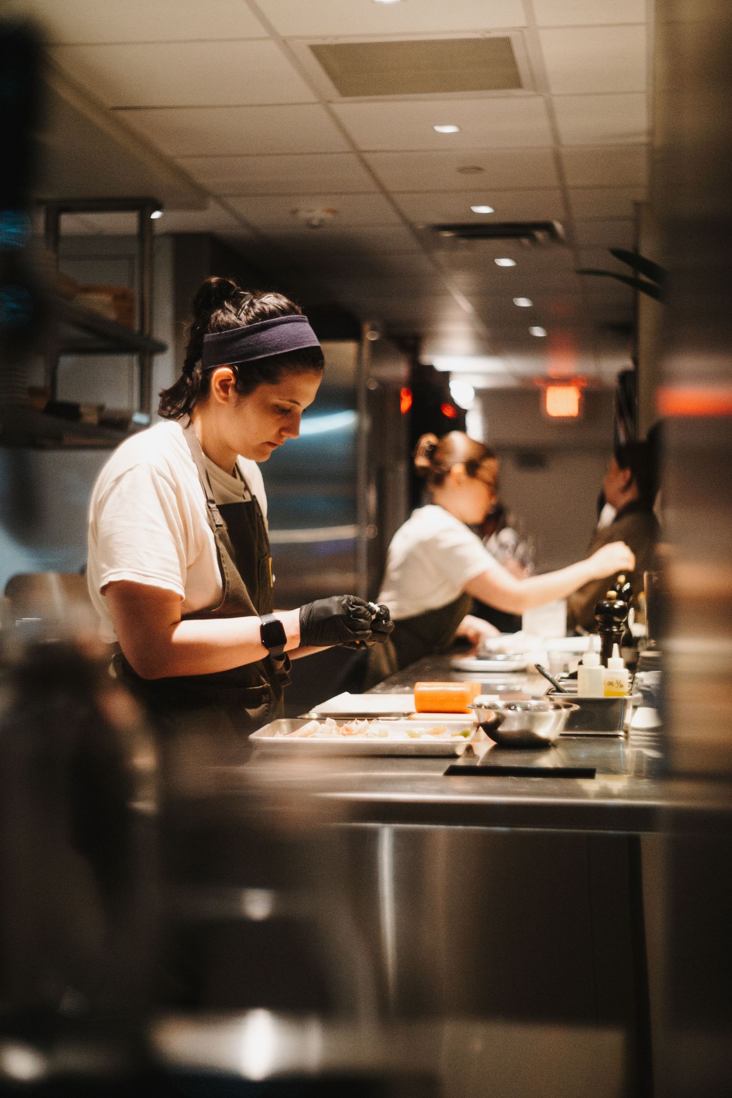 Restaurant kitchen staff preparing food at stainless steel counter with professional equipment in dim lighting.