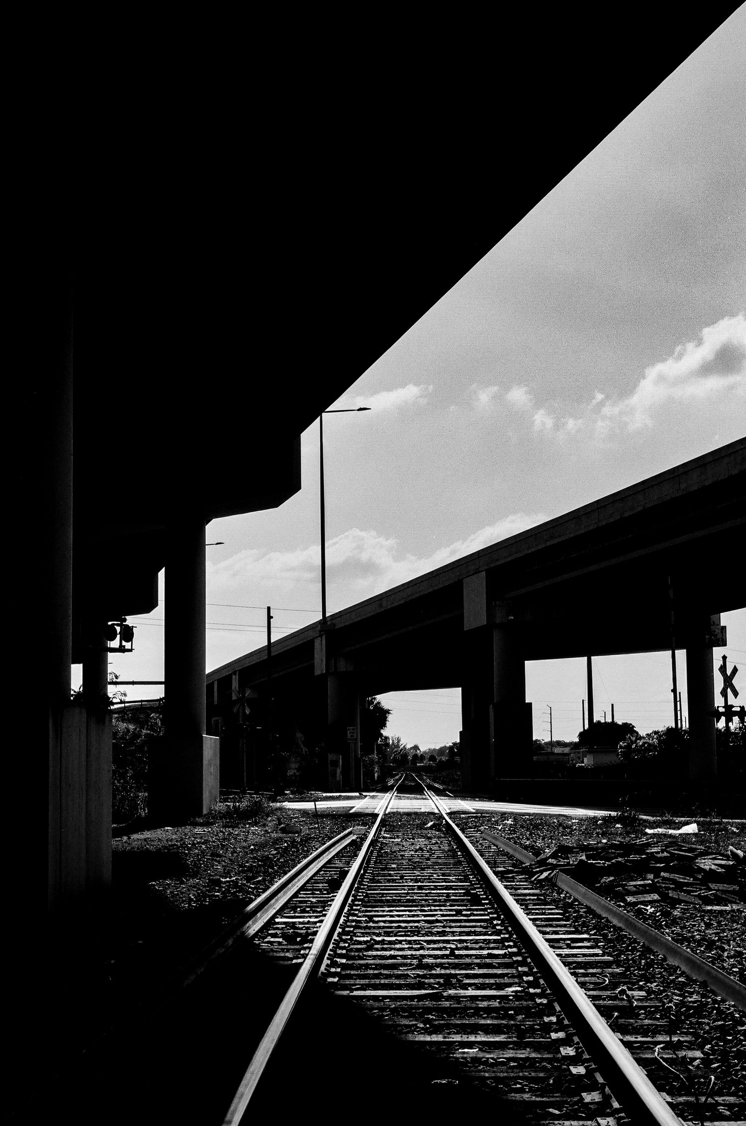 Black and white image of train tracks leading under highway overpasses with dramatic lighting and perspective.