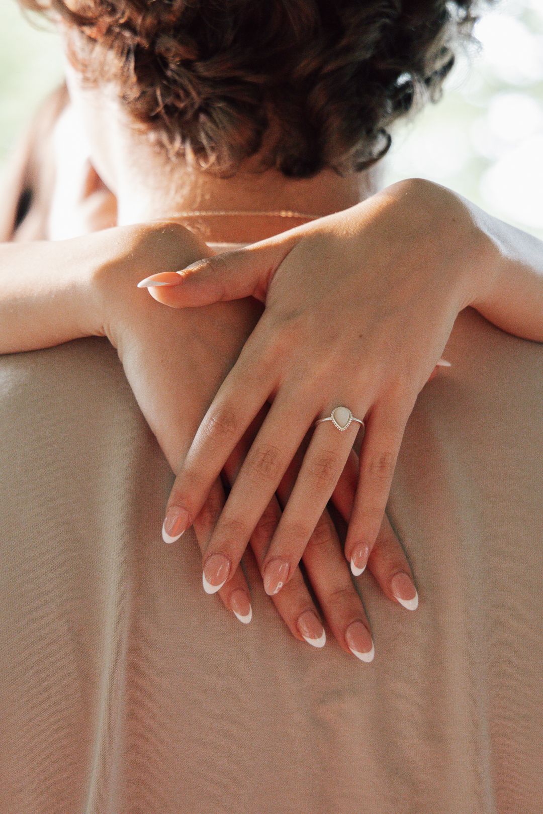 Elegant manicured hands with engagement ring crossed behind back.