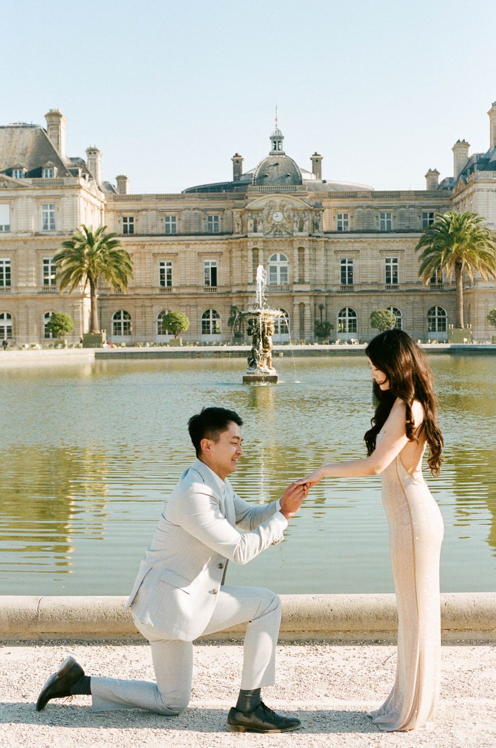 A romantic proposal moment in front of Luxembourg Gardens palace with its grand fountain and palm trees in Paris. paris film photos