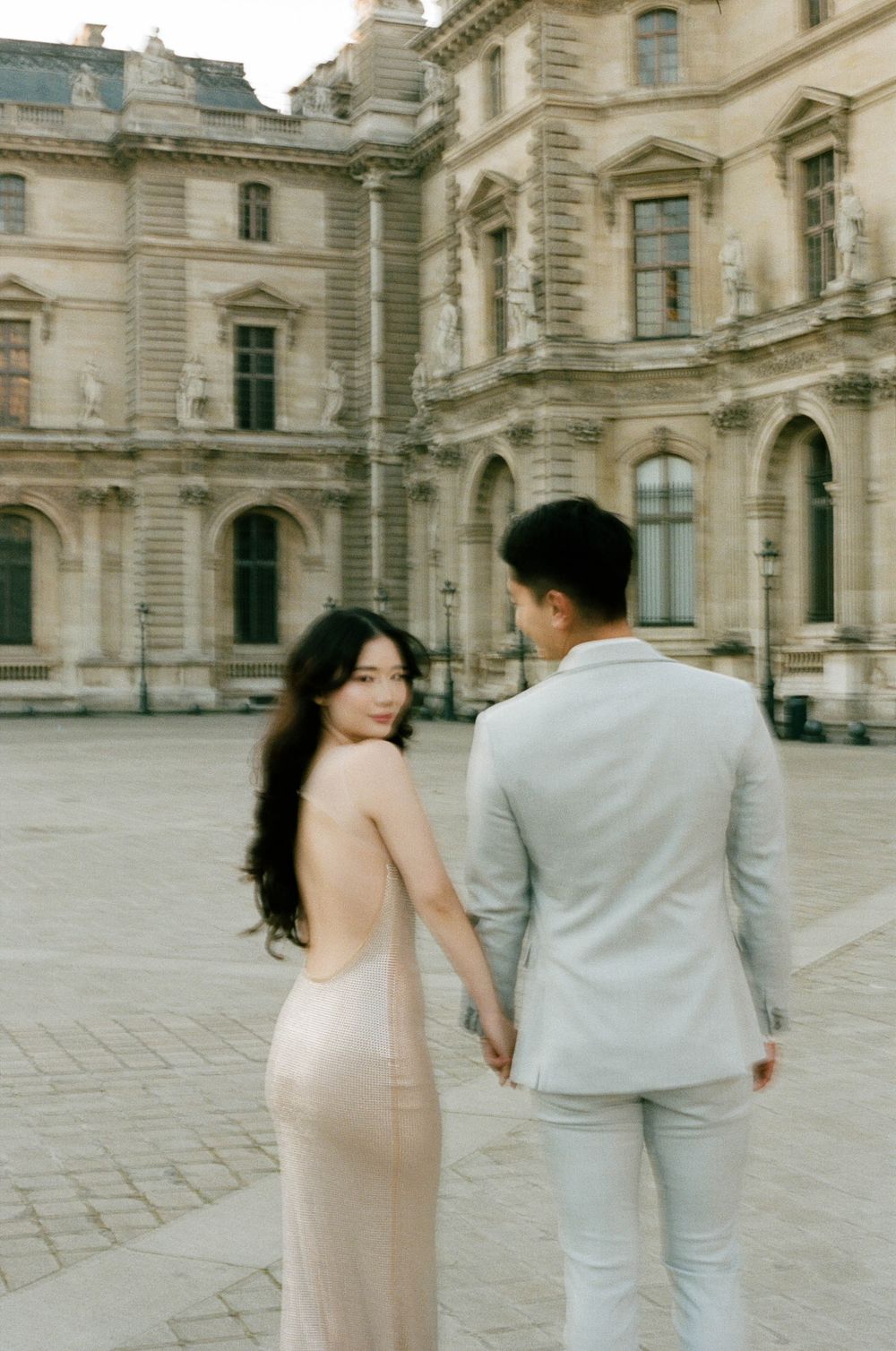 A couple shares a romantic moment in front of a the louvre at sunrise proposal. paris film photoshoot. paris film photographer