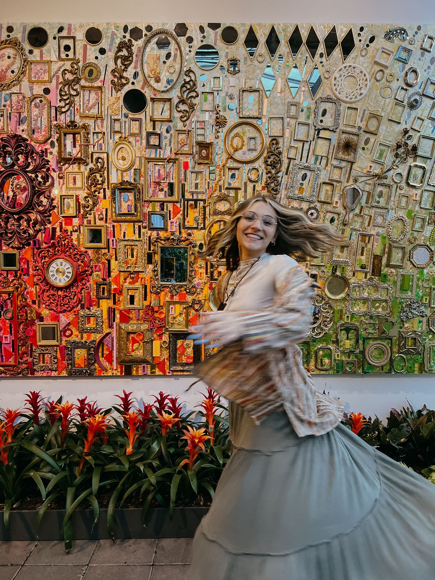 Dancing figure in flowing dress against colorful mosaic wall with red flowers.