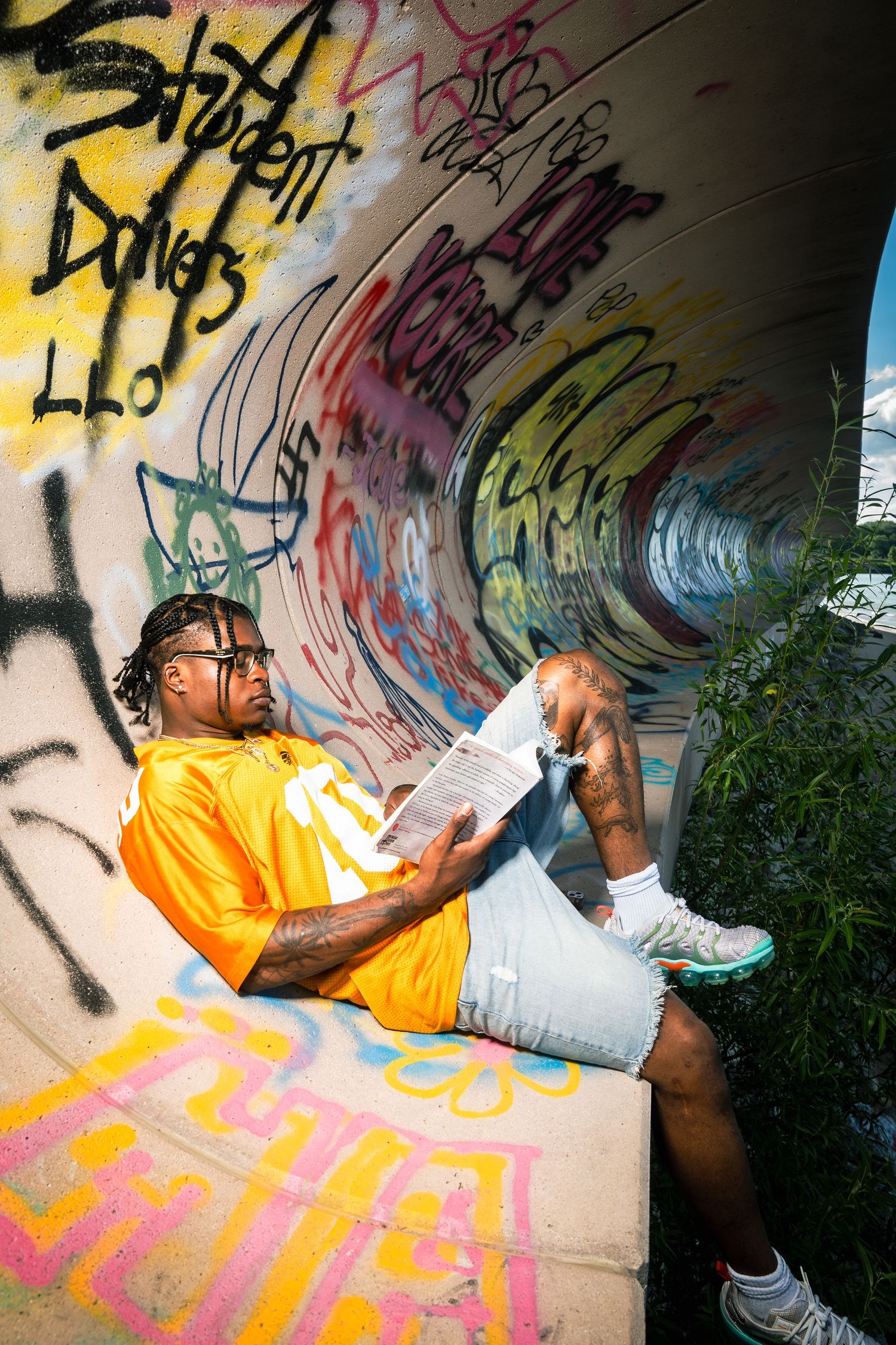 Person in yellow shirt reading while sitting against colorful graffiti wall outdoors.