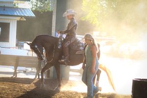 Horse and riders practicing in golden sunset light at an equestrian facility.