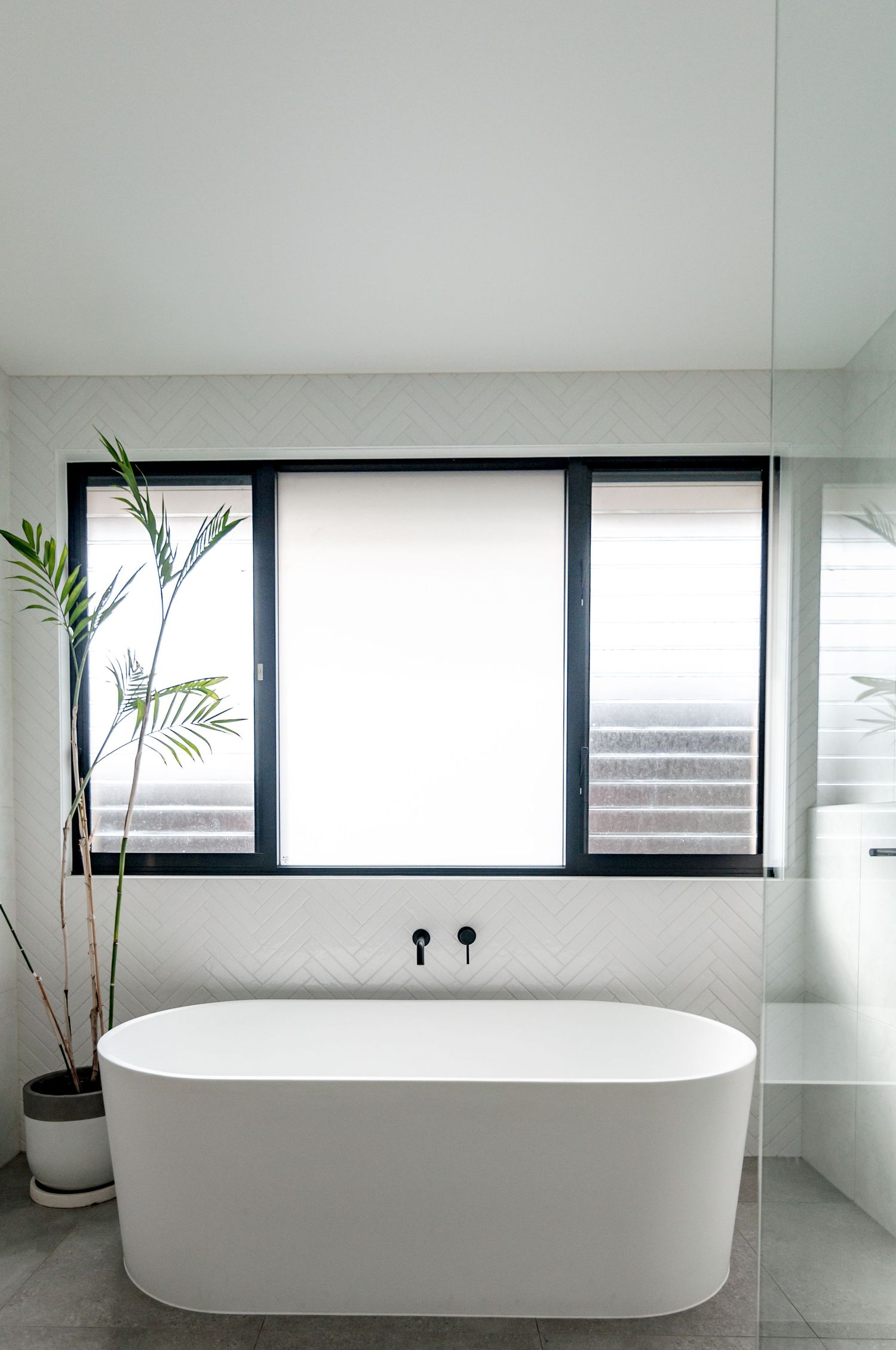 Modern bathroom with freestanding white tub, frosted window, and potted palm plant.