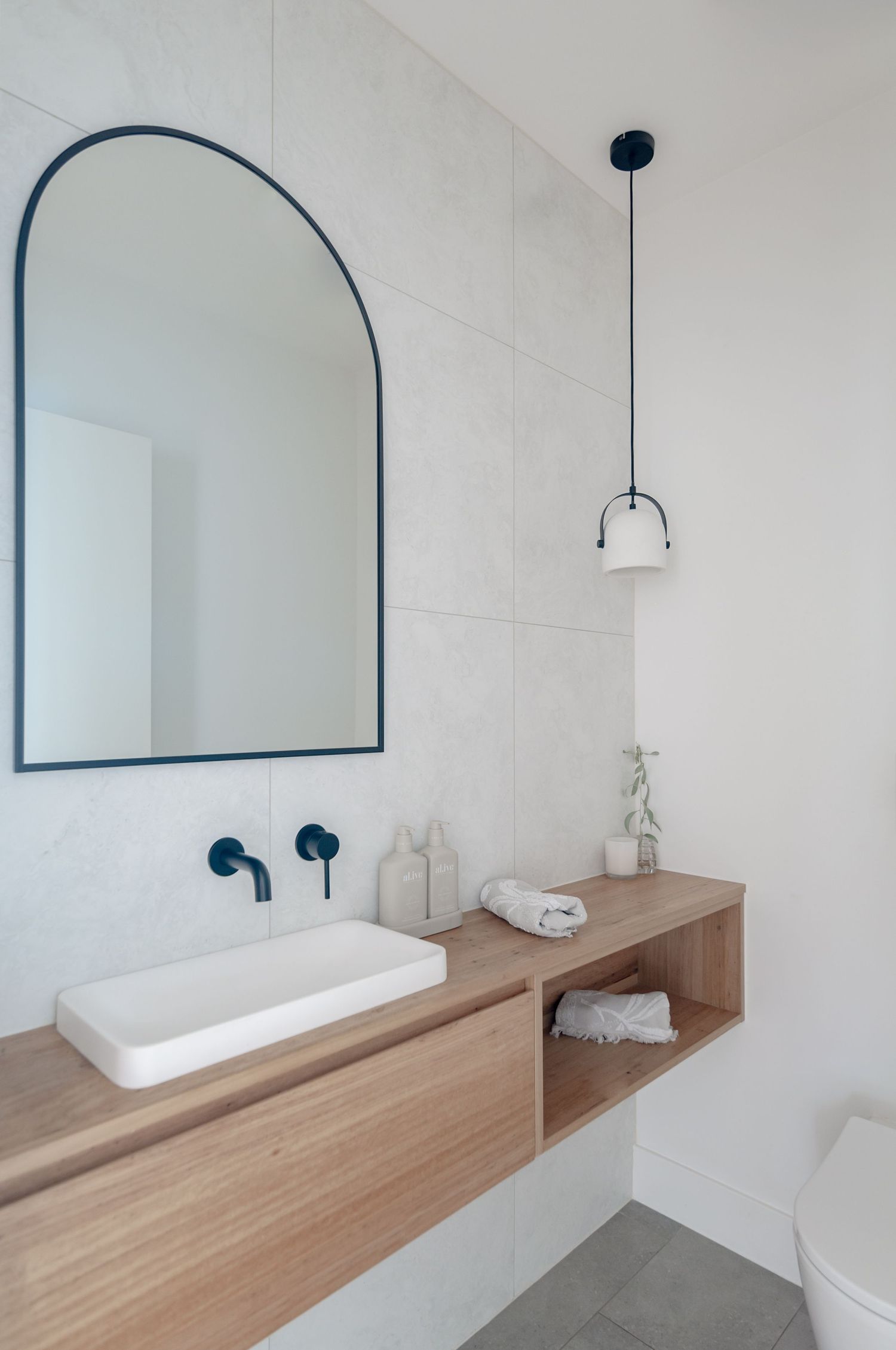 Minimalist bathroom with arched mirror, floating wooden vanity, and pendant light fixture.