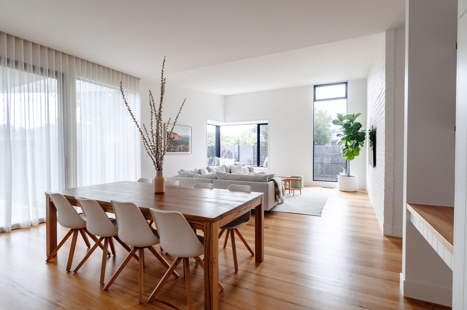 Bright dining area with wooden table, white chairs, and large windows letting in natural light.