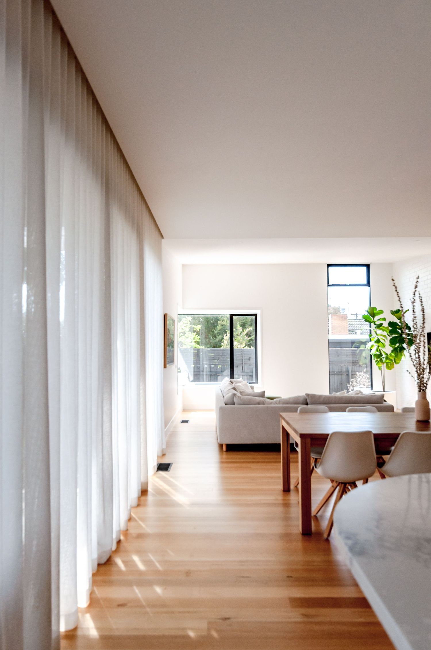 Long hallway with hardwood floors, sheer curtains, and dining area bathed in natural sunlight.