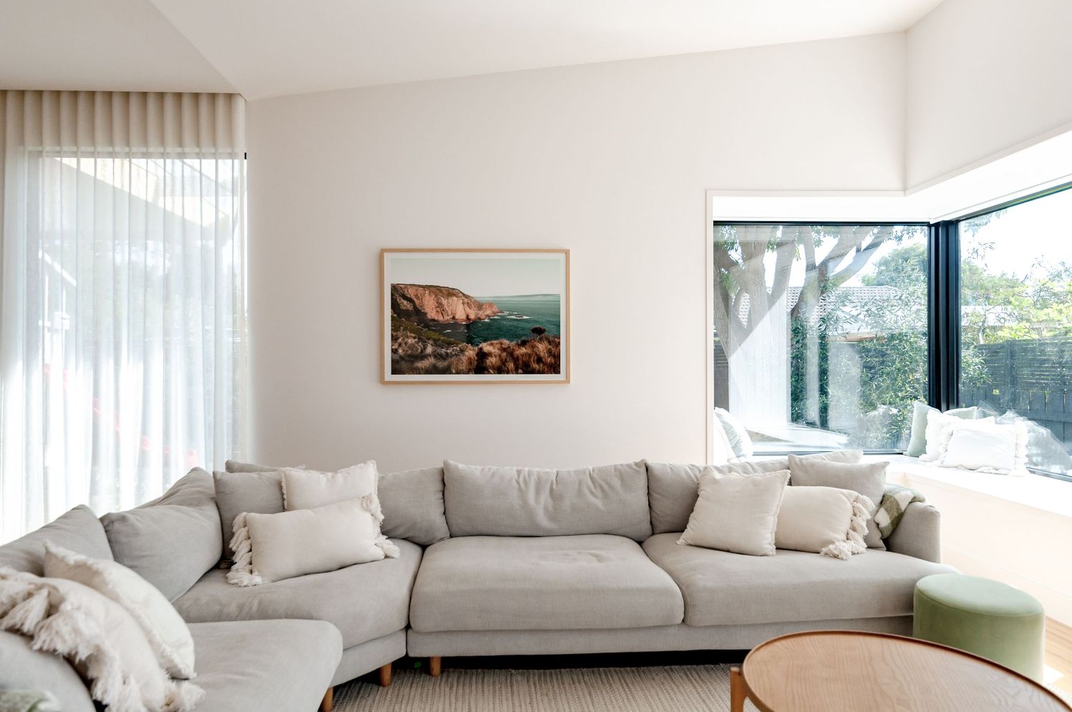 Contemporary living room with grey sectional sofa, coastal artwork, and corner windows.