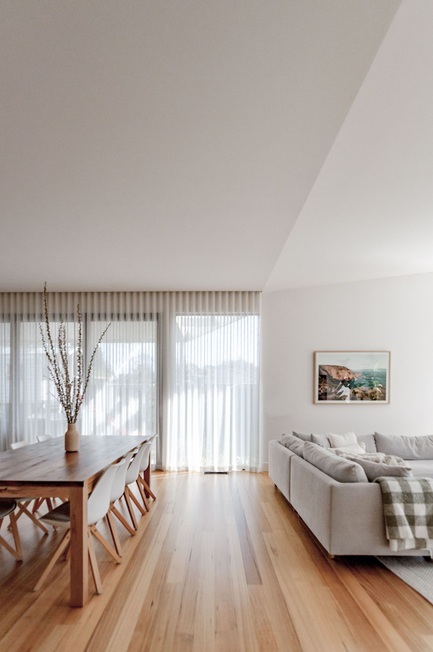 Open-plan living space with hardwood floors, dining table, and floor-length sheer curtains.