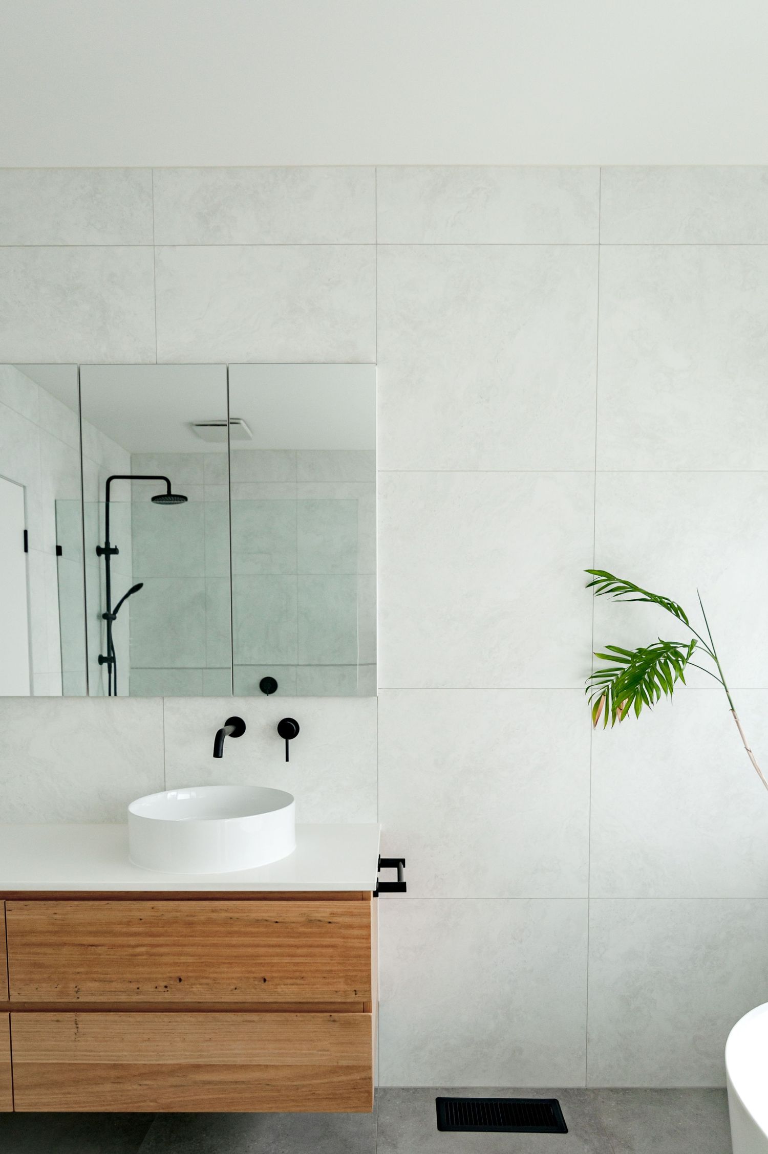 Modern bathroom featuring marble tiles, floating wooden vanity, and black fixtures.