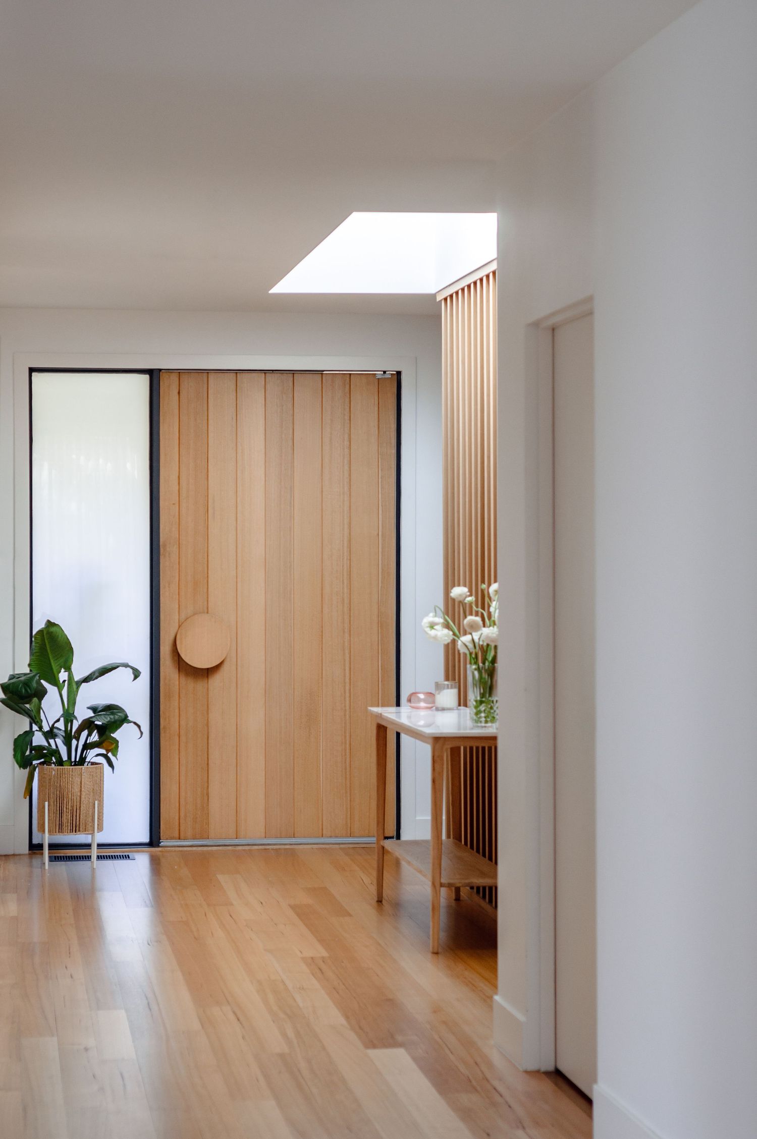 Modern entryway with timber door, skylight, and vertical slat feature wall creating warm natural lighting.