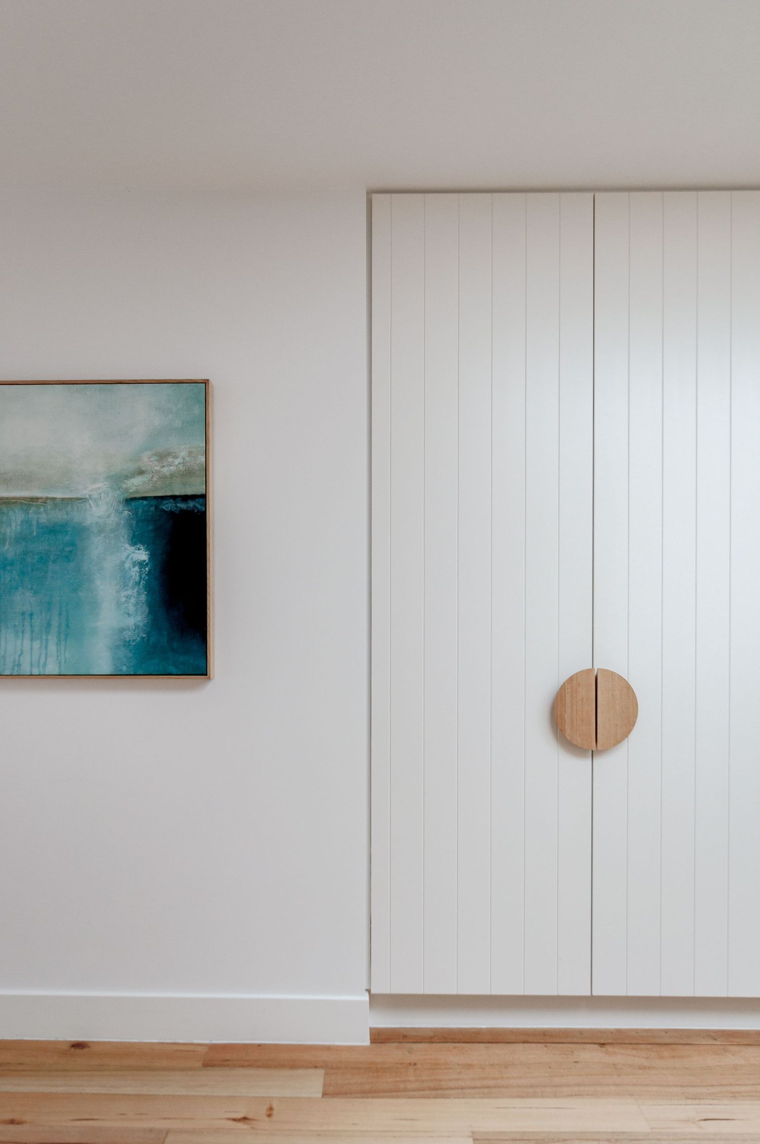 White interior wall with turquoise abstract art and wooden circular door handle.